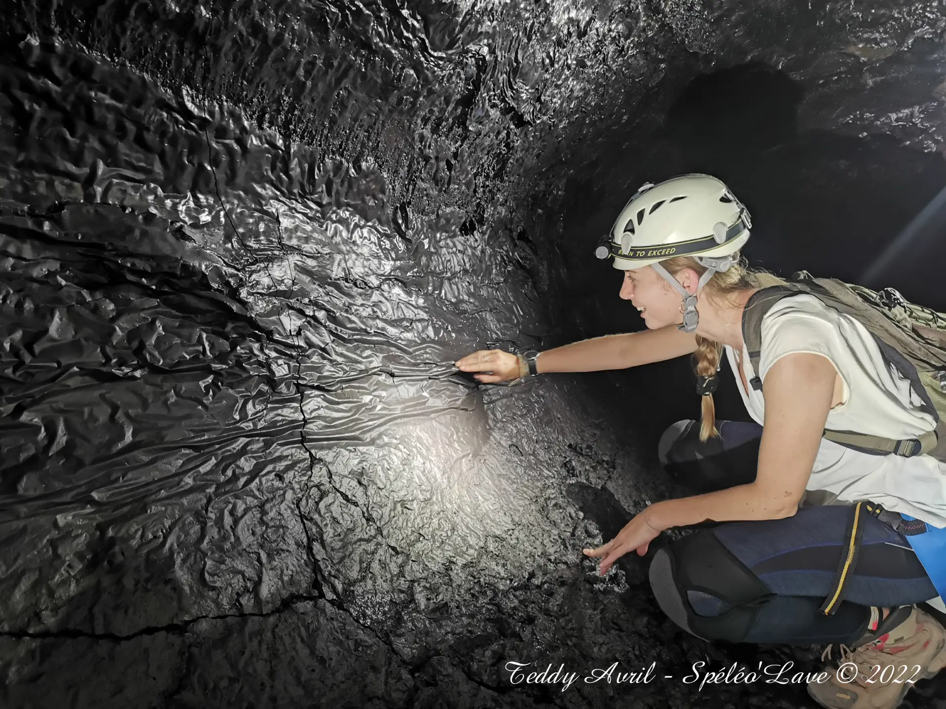 Vaste galerie de tunnel de lave éclairée à la frontale, parois sombres figées par la coulée.