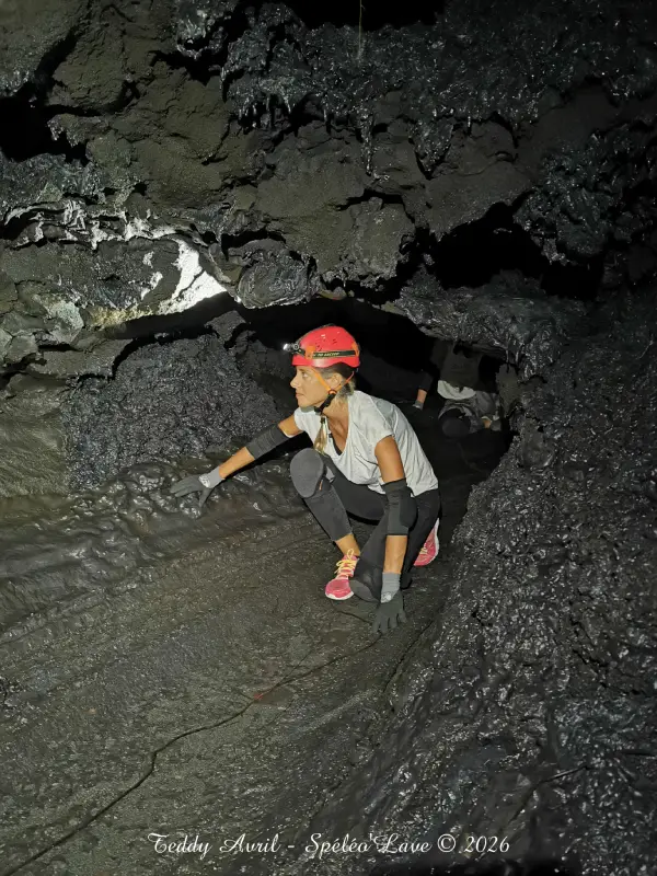Tunnel de lave étroit avec lumière naturelle filtrant depuis un puits, formations volcaniques au plafond.